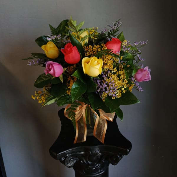 Mixed bouquet of colorful roses in a glass vase with a ribbon
