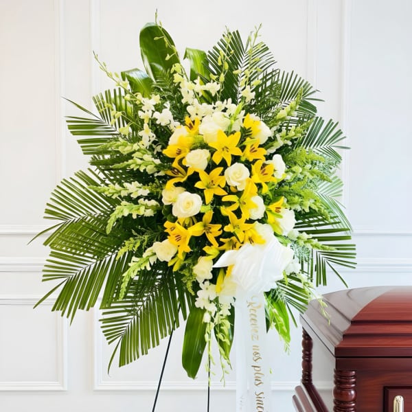 Yellow and white floral standing spray with palm fronds and a white ribbon