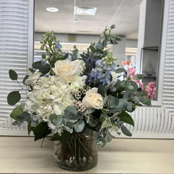 White roses and hydrangea in a glass vase with blue flowers and eucalyptus