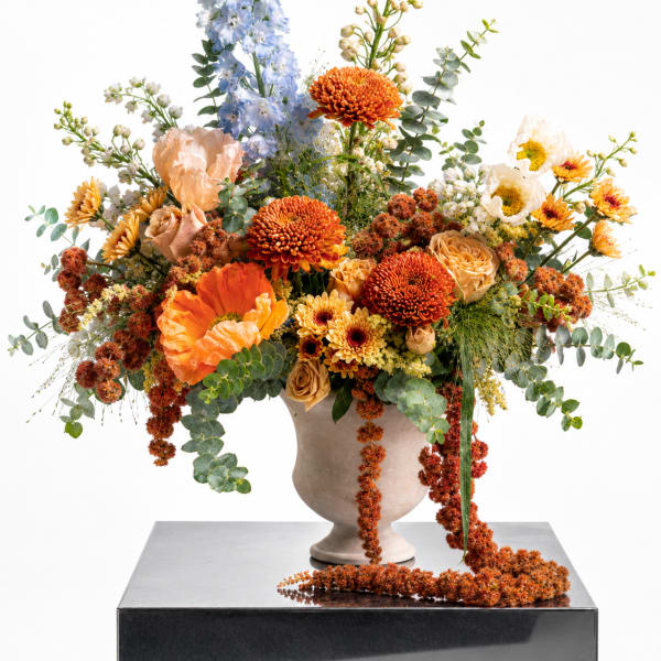 Large mixed floral arrangement in a beige vase with orange, blue, and cream blooms