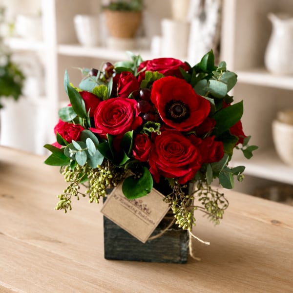 Red rose arrangement in a square vase with eucalyptus and a decorative tag