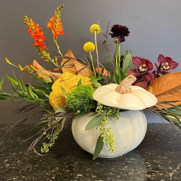 Autumn floral arrangement in a white pumpkin container with orange and burgundy blooms