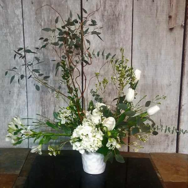 Tall white floral arrangement in a white vase with airy greenery