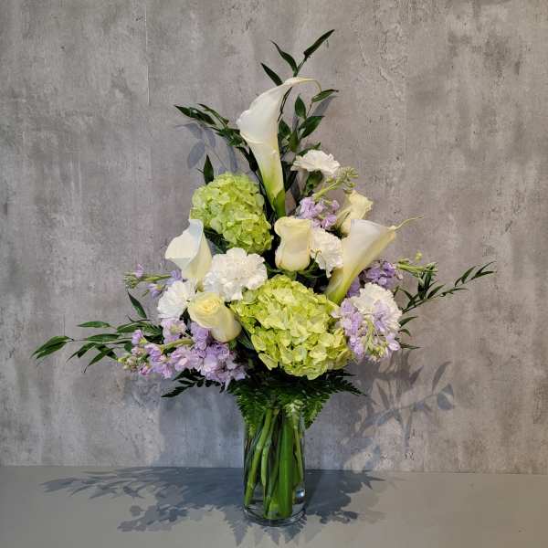 Tall bouquet of white calla lilies, hydrangeas, and lavender flowers in a glass vase