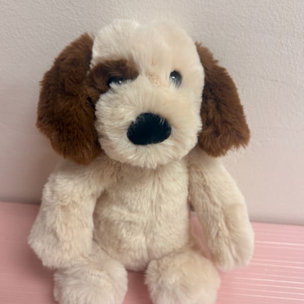 Plush dog toy with cream and brown fur sitting against a pale wall