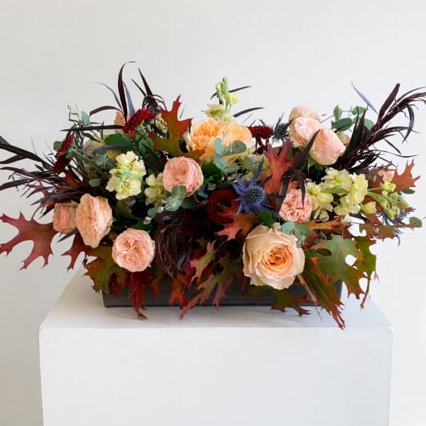 Peach roses and pale yellow flowers in a low rectangular arrangement