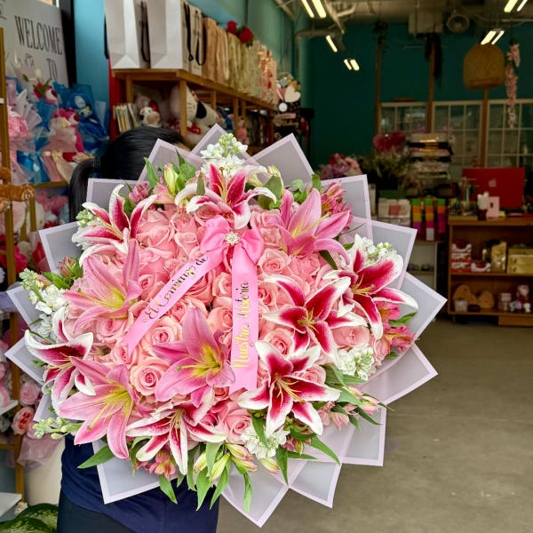 Large pink bouquet with roses and lilies, wrapped in pale paper with ribbons