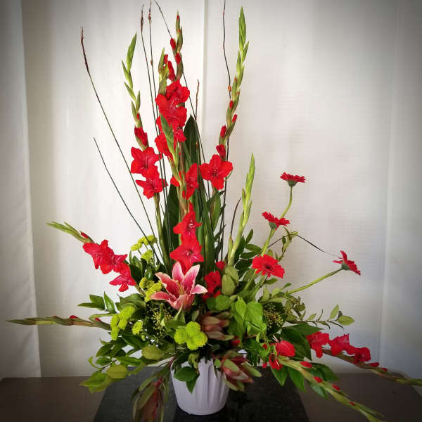 Tall floral arrangement with red gladiolus, pink lily, and green chrysanthemums in a white vase