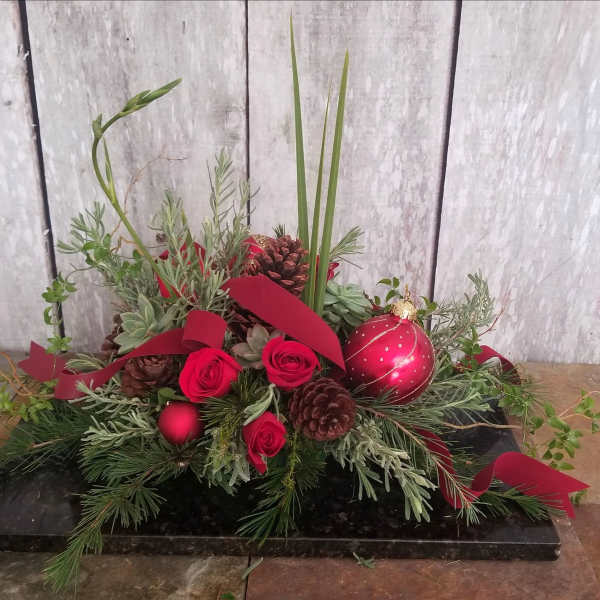 Red roses and pinecones arranged with holiday greenery and a red ornament