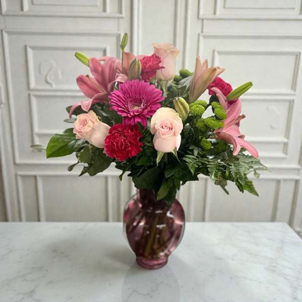 Pink and red mixed flower bouquet in a purple glass vase