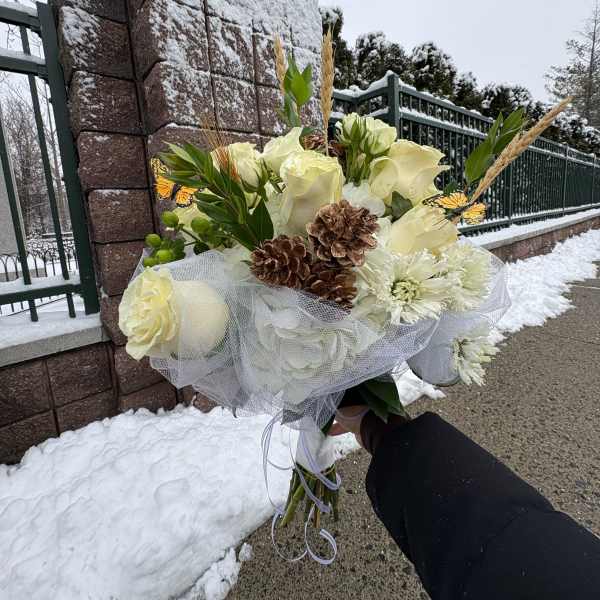 White rose bouquet with pinecones and mesh wrap held outdoors in snow