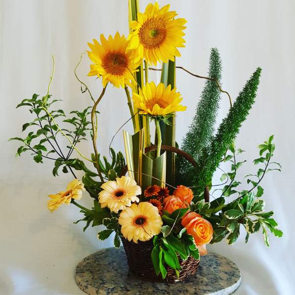 Tall floral arrangement with sunflowers, orange roses, and yellow gerbera daisies in a basket