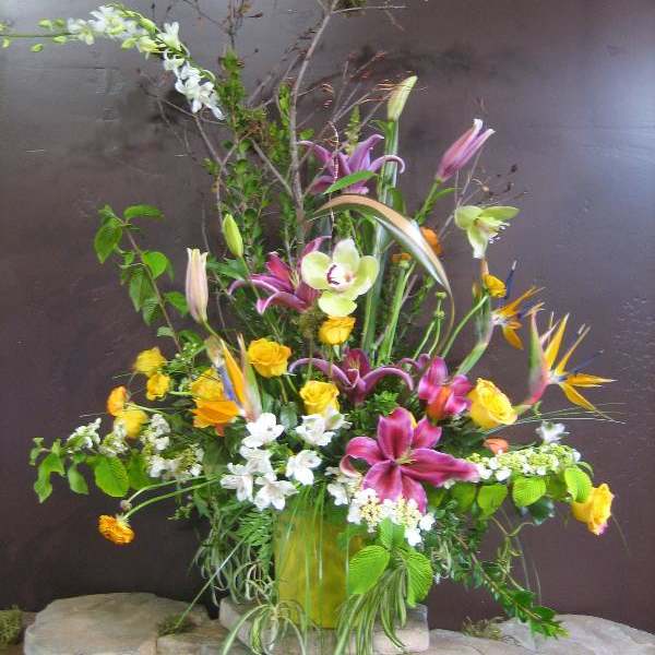 Tall mixed floral arrangement with lilies, roses, orchids, and bird of paradise