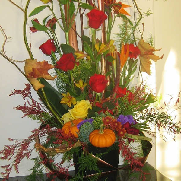 Tall autumn floral arrangement with roses and small pumpkins in a black container