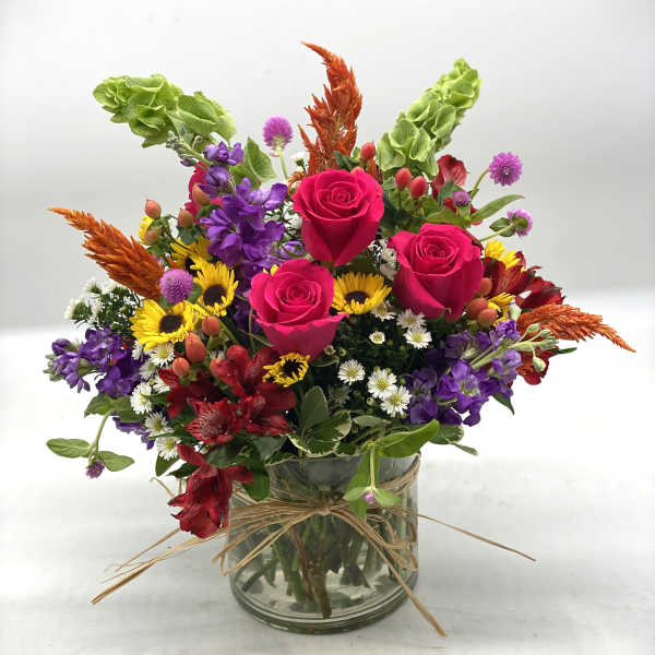 Mixed bouquet of pink roses, purple flowers, and sunflowers in a glass vase