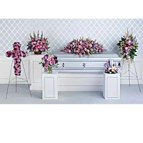 Pink and purple funeral floral arrangements around a silver casket