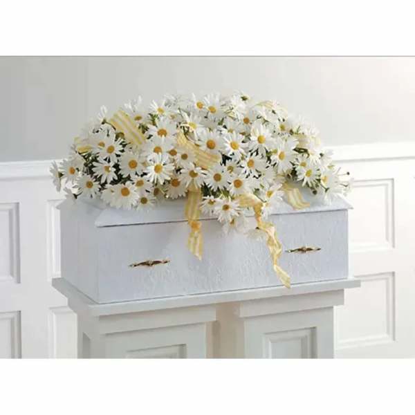 White daisy arrangement on a white casket with yellow ribbon
