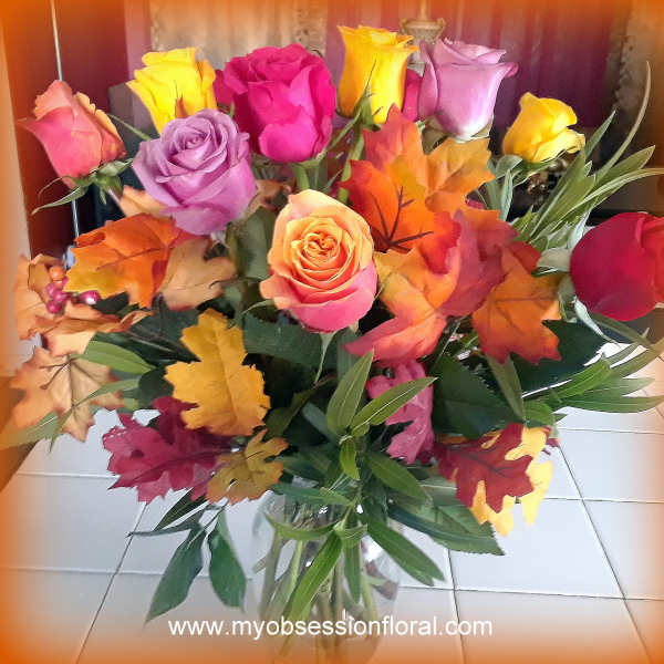 Bouquet of multicolored roses with autumn leaves in a glass vase