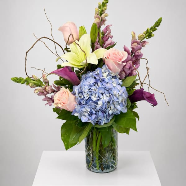 Mixed bouquet in a glass vase with blue hydrangea, pink roses, lilies, and purple blooms