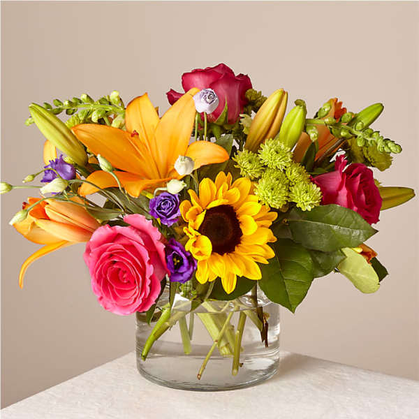 Mixed bouquet with roses, lilies, and a sunflower in a glass vase