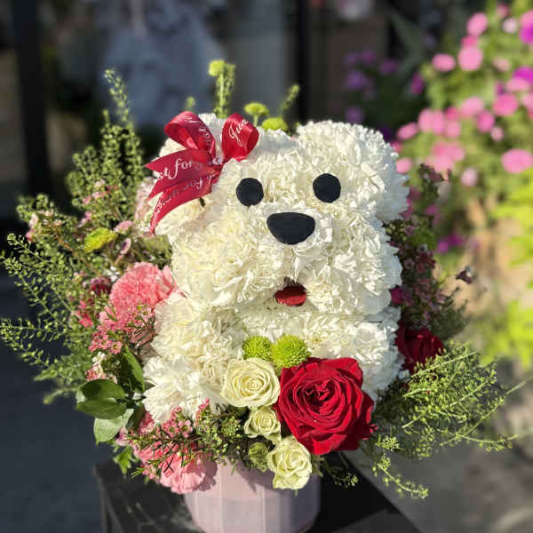 White floral teddy bear arrangement with red roses and a pink ribbon