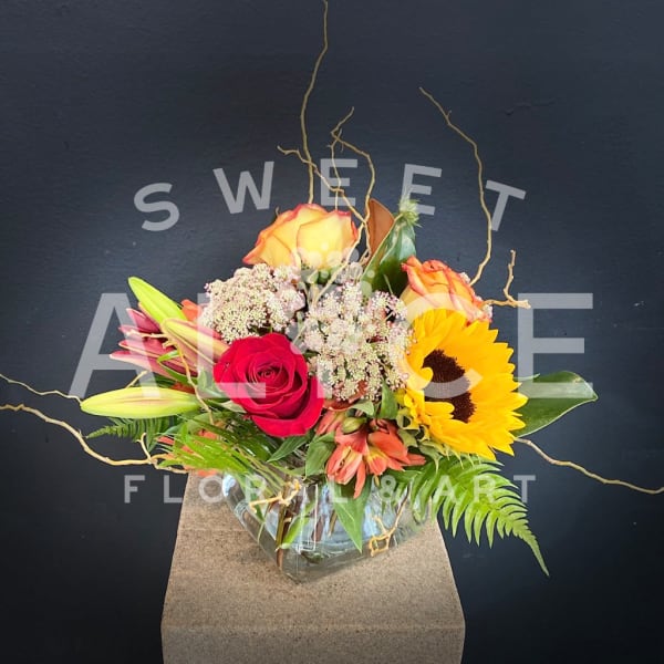 Mixed bouquet with roses, lilies, sunflowers, and alstroemeria in a glass vase