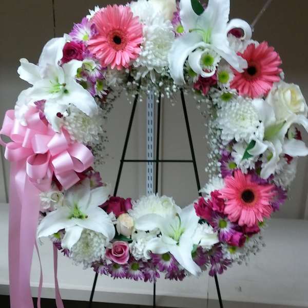 Floral wreath with white lilies, pink gerberas, and a pink ribbon bow
