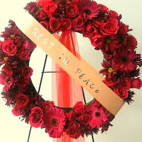 Red floral wreath with a peach ribbon on a stand