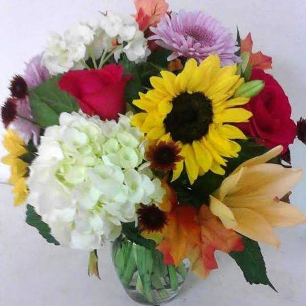 Mixed bouquet with sunflowers, roses, hydrangeas, and lilies in a glass vase