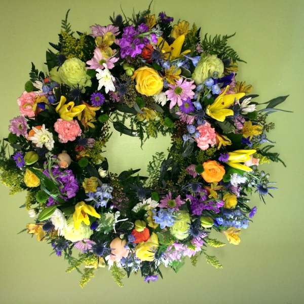 Colorful floral wreath with roses, lilies, and daisies on a green background