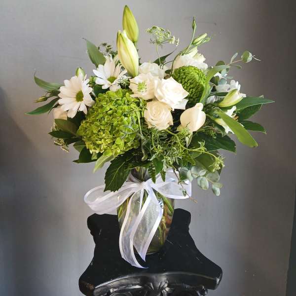 White and green floral arrangement in a glass vase with a white ribbon