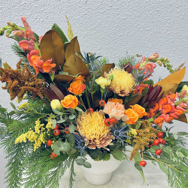 Autumn floral arrangement in a white vase with orange and yellow blooms