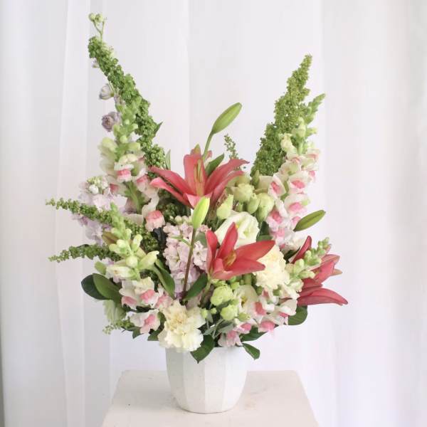 Tall mixed flower arrangement in a white vase with pink and white blooms