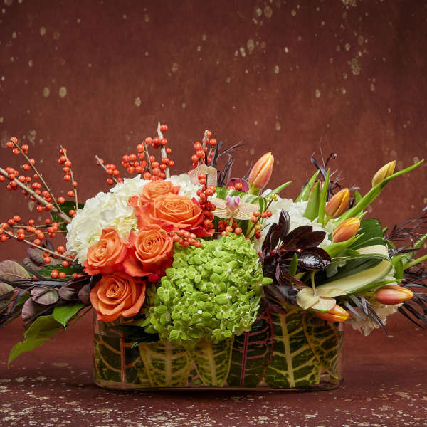 Mixed floral arrangement with orange roses, white hydrangeas, and tulips in a patterned container