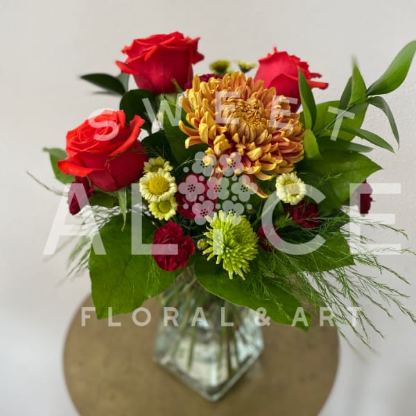 Bouquet of red roses and mixed mums in a glass vase