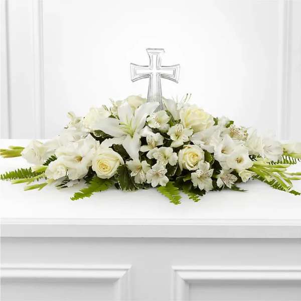 Low white floral spray with lilies and roses accented by a clear cross ornament.