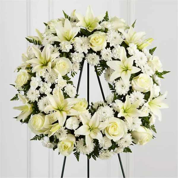 White sympathy wreath of lilies, roses, and mums displayed on a metal easel stand