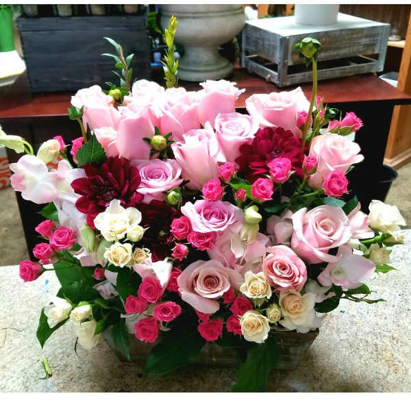 Pink and white rose arrangement with burgundy blooms in a low container