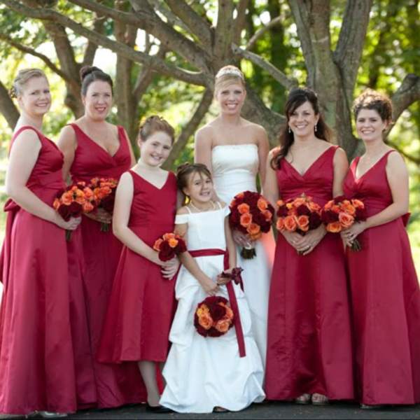 Bridal party in red dresses holding orange and burgundy bouquets