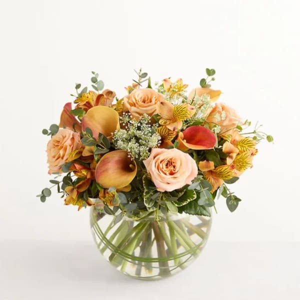 Peach and yellow flower bouquet in a round glass vase