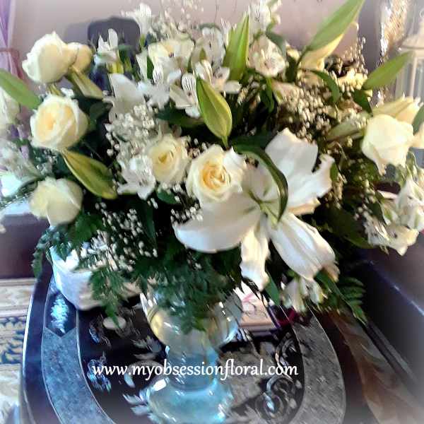 Large white floral arrangement with roses and lilies in a glass vase