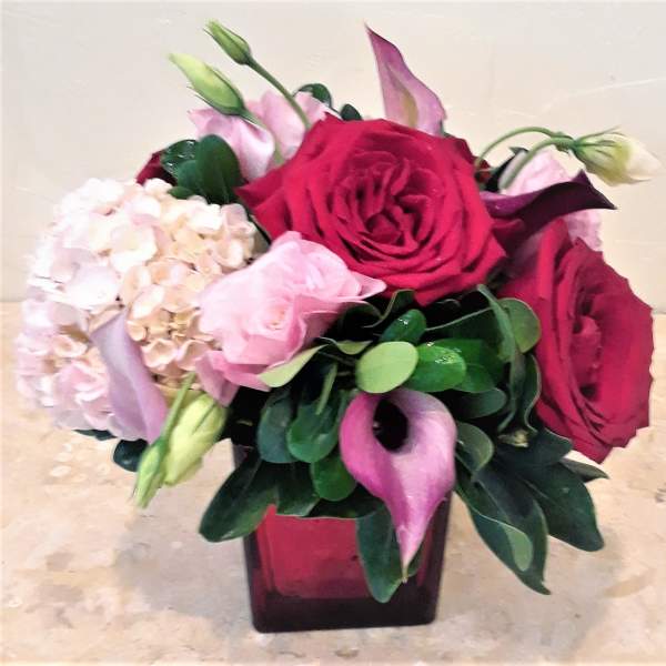 Bouquet of red roses, pink hydrangea, and calla lilies in a square vase