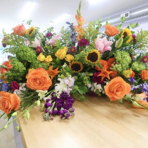 Large mixed floral arrangement with orange roses, sunflowers, and lilies on a table