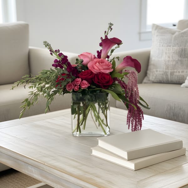 Pink and burgundy floral arrangement in a clear glass vase on a coffee table