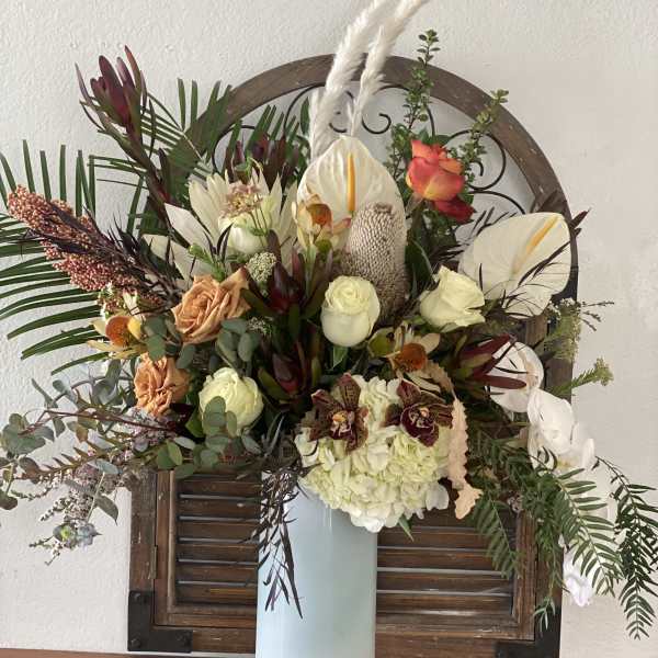 Large mixed floral arrangement in a tall white vase with white anthuriums and roses