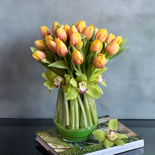 Peach and yellow tulips with green orchids in a clear glass vase set on two books