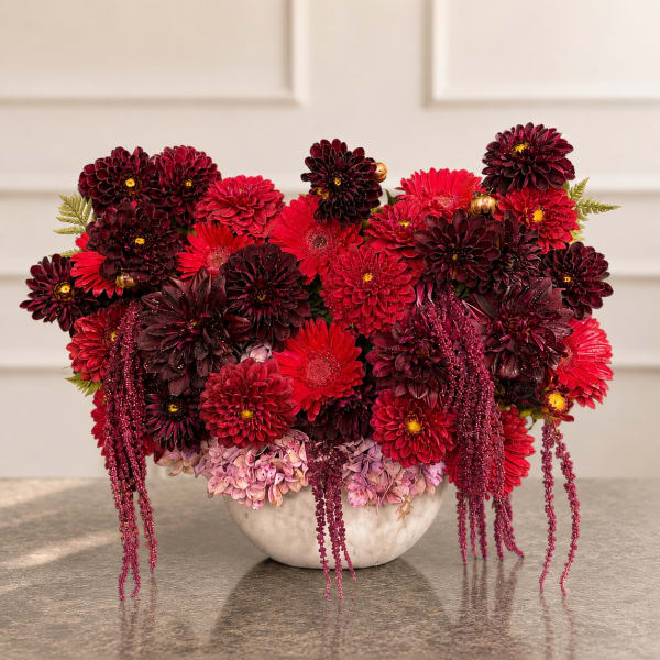 Red and burgundy flower arrangement in a white bowl vase