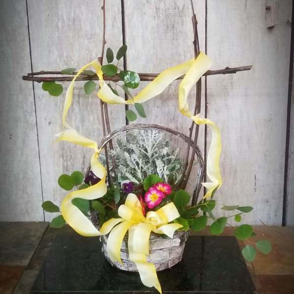 Basket arrangement with pink flowers, greenery, and yellow ribbon on a twig frame