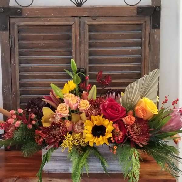Colorful mixed flower arrangement in a rectangular container with a rustic window backdrop