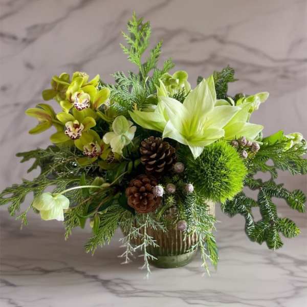 Green floral arrangement with orchids, lilies, and pinecones in a glass vase